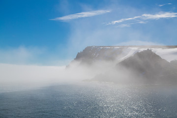 High sea rocks in snow and a fog.