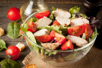 Fresh salad made of tomato, ruccola, chicken breast, arugula, crackers and spices. Caesar salad in a white, transparent bowl on wooden background
