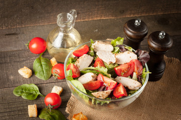 Fresh salad made of tomato, ruccola, chicken breast, arugula, crackers and spices. Caesar salad in a white, transparent bowl on wooden background