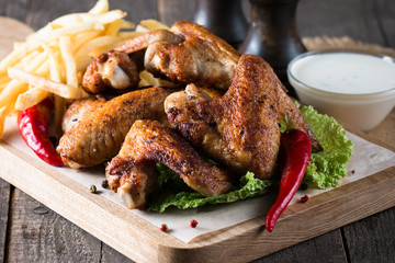 Close-up photo of bbq chicken wings with fries and beer. Barbeques meat with sauces, ketchup, mayonnaise. Fast and junk food concept. 