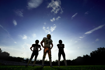 Players in American football are on the field against the sky at sunset.