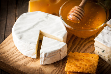 Slate board with various cheese and a glass of red rose wine. Brie. Camembert. Gouda, Masdaam, Roquefort, Cheddar and grapes on a wood with nuts, honey, crackers, blue cheese. Italian, French cheese.