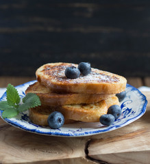  Stack of homemade French toast sprinkled with blueberries  on a blue plate on a wooden texture board. tasty breakfast.