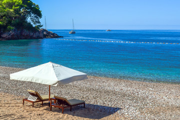 Idyllic scene of deck chairs under an umbrella on a clean beach in the hot afternoon sun.