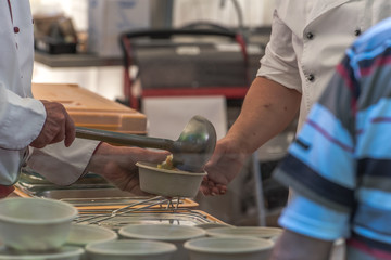 Cook serving soup with sausages in a bowl from the big cauldron in the outdoor festival