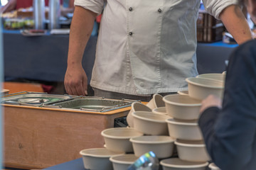 Cook serving soup with sausages in a bowl from the big cauldron in the outdoor festival