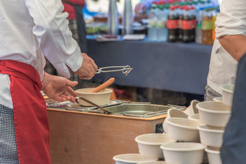 Cook serving soup with sausages in a bowl from the big cauldron in the outdoor festival