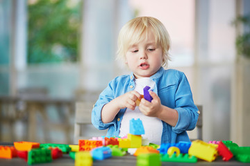 Little boy playing with colorful plastic construction blocks