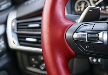 Obraz na płótnie Canvas Cruise control buttons on the red steering wheel of a modern car, car interior details