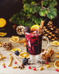 glass of hot mulled wine for the new year with ingredients for cooking, nuts and Christmas decorations