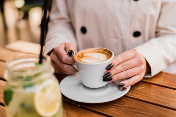 Female hands holding a cup of coffee with foam over wooden table.