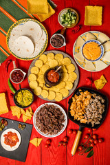 Mexican food concept: tortilla chips, guacamole, salsa, chilli, refried black beans, pulled beef, chicken, cheese and fresh ingredients over vintage red rustic wooden background. Top view
