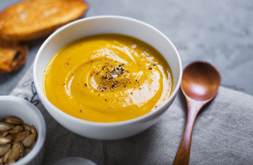 Roasted pumpkin and carrot soup with black pepper and pumpkin seeds on grey concrete background. Close up. Side view. Copy space