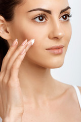 Fototapeta na wymiar Facial Care. Female Applying Cream.Portrait Of Young Woman With Cosmetic Cream On Skin. Closeup Of Beautiful Girl With Beauty Product On Soft Skin, Natural Makeup Touching Face. High Resolution