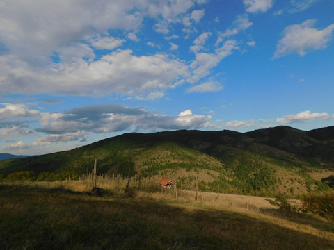Mountain landscape, cottage, cloudy sky, sunny day.