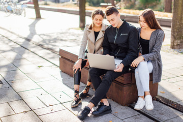 Three friends sit on the bench with laptop