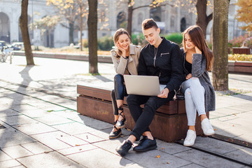 Three friends sit on the bench with laptop
