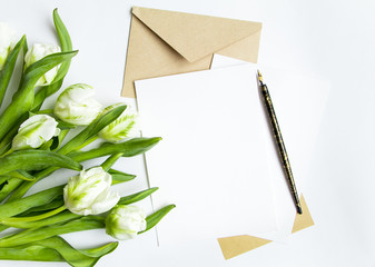 Letter, envelope and bouquet on white background. Invitation cards, or love letter with white tulips. Top view, flat lay