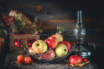 Autumn still life of apples in a basket with a lamp and candles.