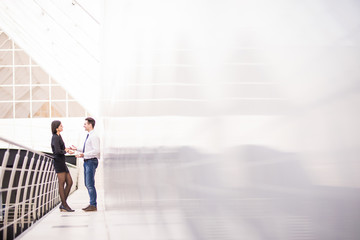 Two happy businesspeople standing in front of office windows, talking and smiling. Team work