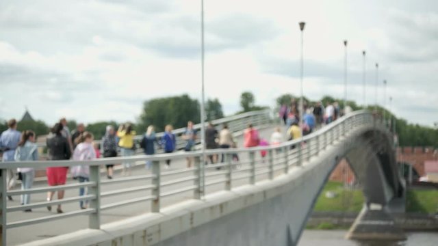 Blurred crowded pedestrian bridge video with bokeh. People walking on pedestrian bridge over river in summer season
