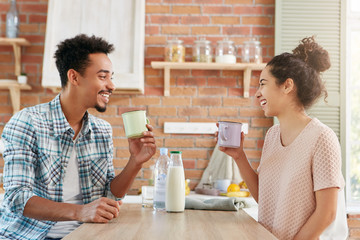 Fototapeta na wymiar Spending time at home together. Cheerful bearded man and his wife drink tea or milk in morning, have good mood, being glad to have vacations and not go for work. Pleasant conversation between lovers