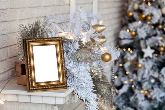 White empty photo frame on the fireplace. Christmas white interior background with bokeh defocused effect