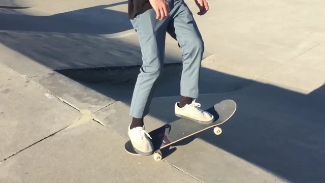 Skateboarder approaches in slow motion with bright sunlight illuminating his lower body as he starts his descent into empty pool at skate park.