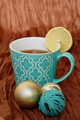 Turquoise mug with pattern filled with tea and slice of lemon with brown background 