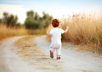 cute toddler baby boy running away along the path at summer field
