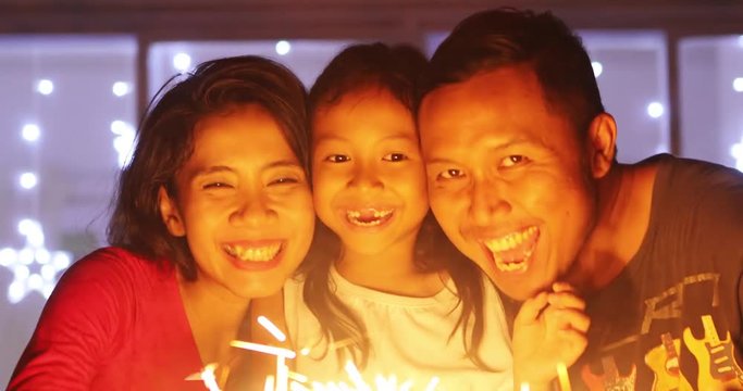 Two happy parents and their toothless daughter playing Christmas sparklers at home, shot in 4k resolution