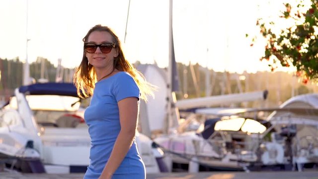 Woman in sunglasses walking along the dock with a lot of yachts and boats at sunset