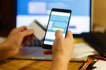 Male hand holding a mobile phone and payment by credit card. Online payments and purchases. The banking application is opened on a smartphone.