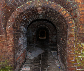 Dark brick tunnel of the catacomb with arched entrance view to the darkness of the old building