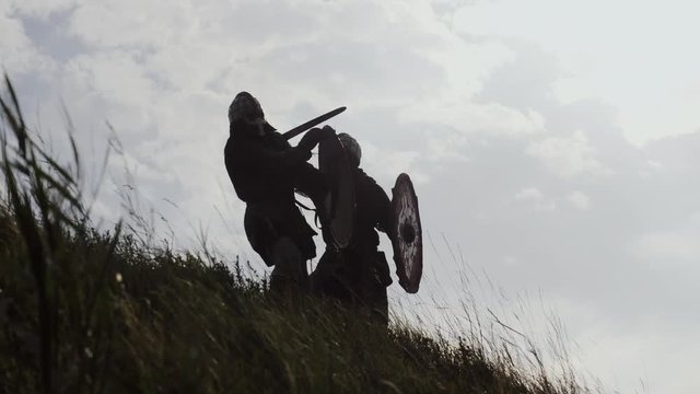 Silhouettes of two warriors Viking are fighting with swords and shields.