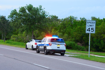 Police truck suv vehicle with flashing red and blue lights has pulled over a sports car for speeding and they happen to be on the side of the road by a speed limit sign. - 177587934