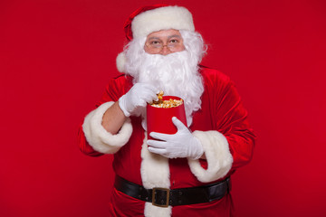 Traditional Santa Claus watching TV, eating popcorn. Christmas. Red background. emotions fear surprise