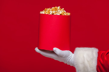 Christmas. Photo of Santa Claus gloved hand With a red bucket with popcorn, on a red background