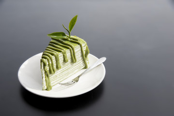 Japanese Matcha Green tea cake with tea leaves in white plate on modern black table in background