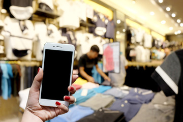 Women hold a smartphone in the mall's clothing store. Have background blurred images.