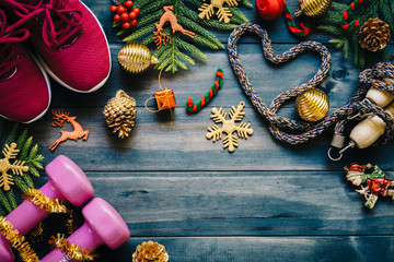 Exercise, Fitness and Working Out Merry Christmas and Happy new year concept, dumbbells, sport shoes, skipping rope or jump rope  in heart shape with Christmas decoration items on wood background. 