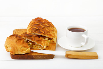 Strudel with apples and cinnamon, cup of tea and knife on white wooden table. Shallow focus.