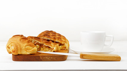 Strudel with apples and cinnamon, cup of tea and knife on white wooden table. Shallow focus.