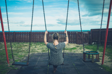 Young woman sitting on a swing by the sea