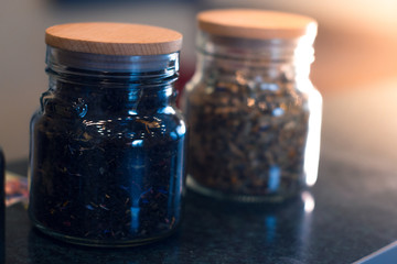 Different types of tea in glass jars on a blurred background.