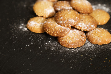 Small round cookies with sesame dusted with powdered sugar on dark background.