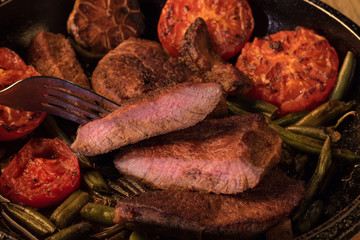Grilled steak, sliced in half on a cast iron skillet with slices of fried red tomatoes and French beans