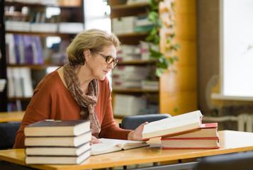 An elderly woman is studying for the exam in the library