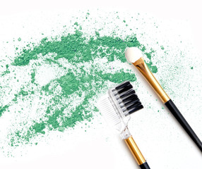 Green make up eyeshadow crushed and brushes on white.