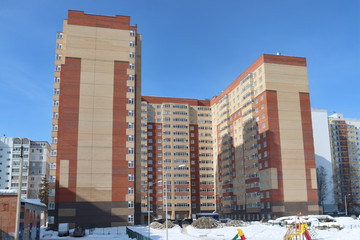 Multi-storey residential building on background of blue sky and childrens playground in winter